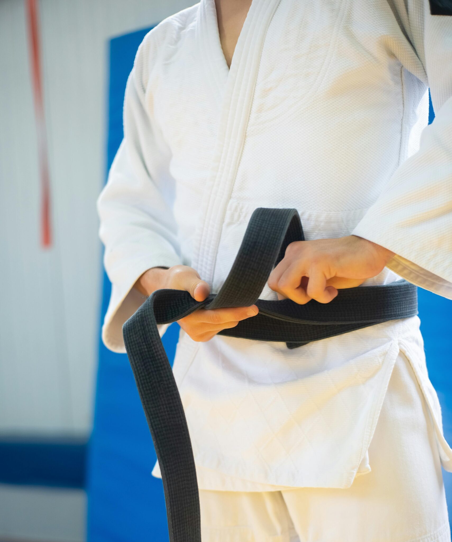 Close-up of a judoka in white uniform tying a black belt, indicating discipline and skill.